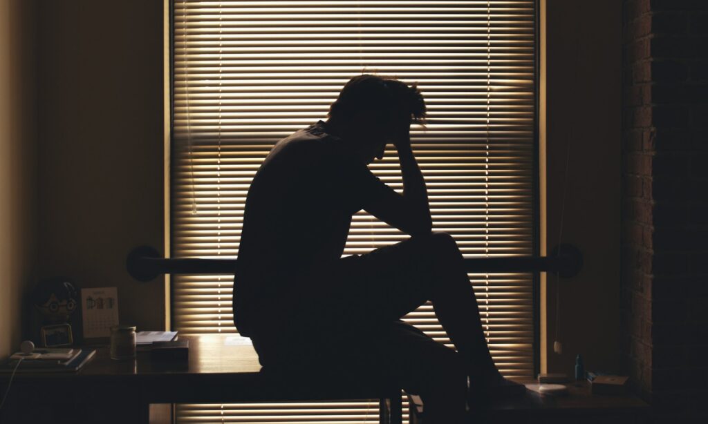 A Man With Anxiety Sitting in a Dark Room With Hand on his head, Stitha Prajna